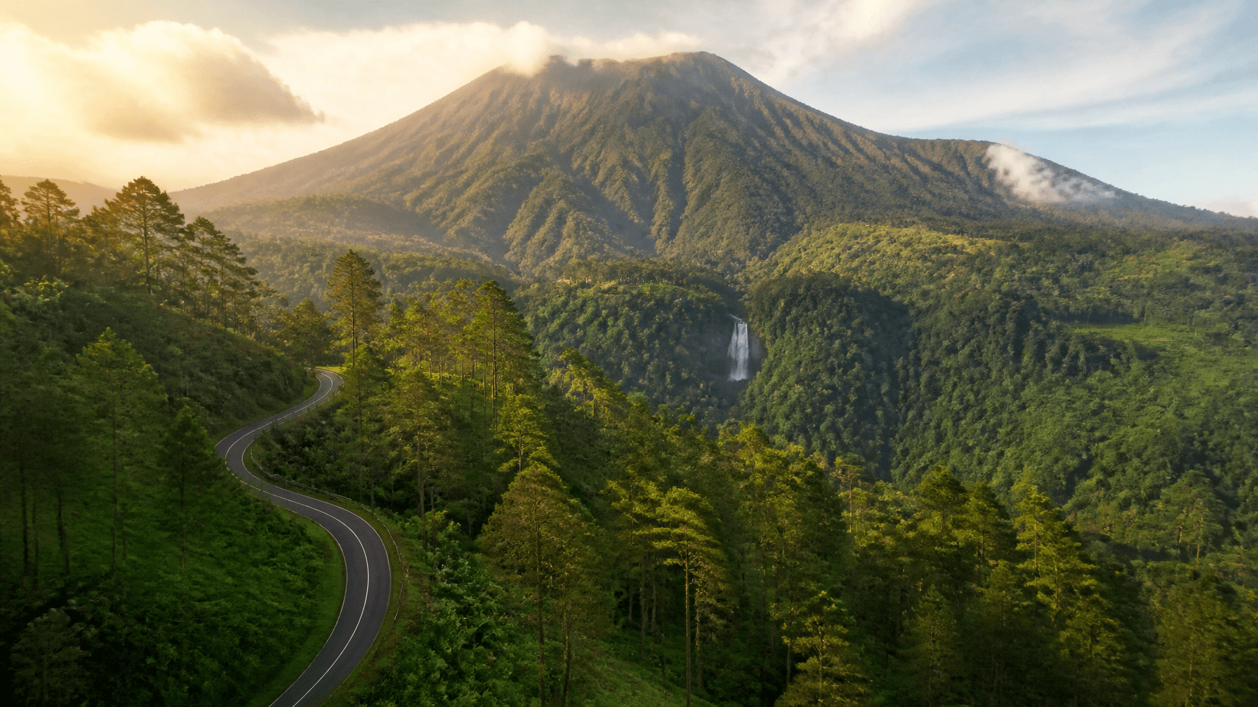 A stunning wide landscape photo of Baturraden mountain with lush green pine forests and a winding ro
